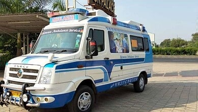 Blue and white ambulance parked outdoors with trees and a building in the background.