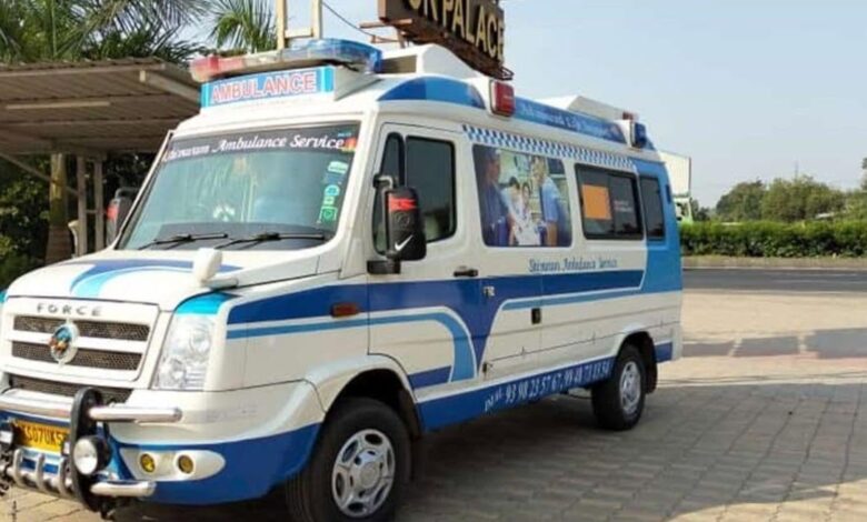 Blue and white ambulance parked outdoors with trees and a building in the background.