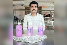 Man sitting behind bottles labeled 'RA', 'CP', and 'LH' with cash in front, in an indoor setting.