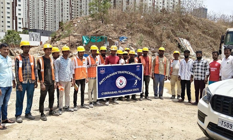 Group of construction workers and officials holding a Hyderabad police banner at a construction site.