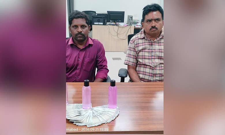 Two government officials detained in Nizamabad for Rs 15,000 bribe, seated at a table.