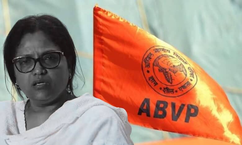 Muslim woman vice-principal speaking at an event with ABVP flag in background.