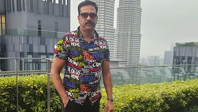 Man in colourful shirt and sunglasses standing on rooftop with cityscape background.