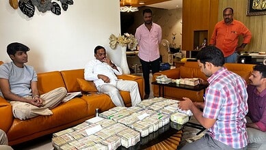 Group of men sitting around a table with stacks of cash in a living room.