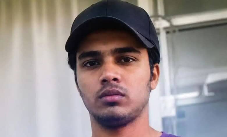 Young man with serious expression wearing a black cap indoors.