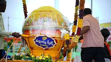 Large decorated Ganesh idol during a festival with flower garlands and people around.