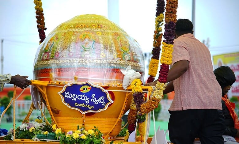 Large decorated Ganesh idol during a festival with flower garlands and people around.