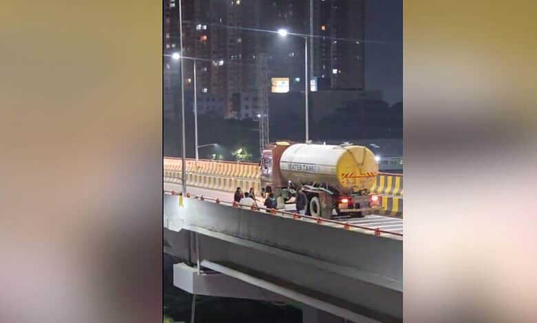 Women dancing on Bachupally flyover at night, with city lights in the background.