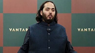 Anant Ambani speaking at an event with a VANTAA backdrop behind him.