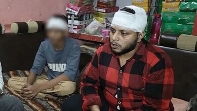 Man with bandaged head sitting with a young boy in a shop with stacked goods behind them.
