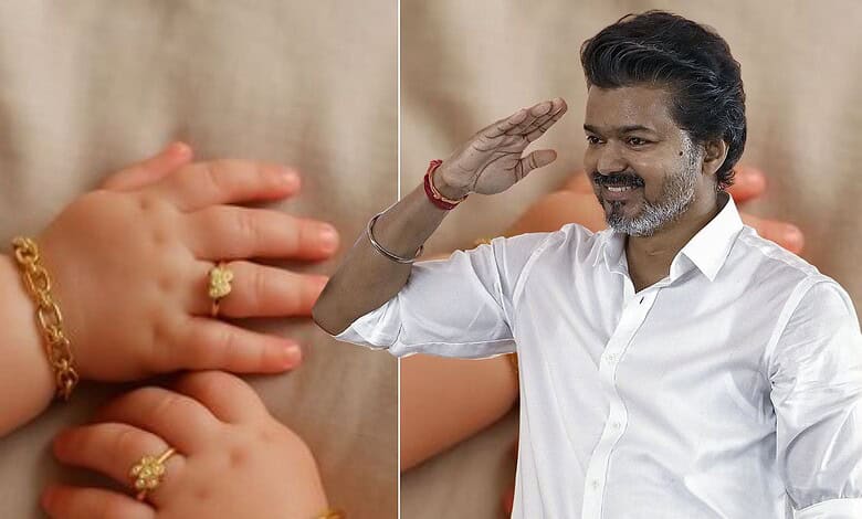 Indian man saluting with a smile, wearing a white shirt, with a background of children and gold jewelry.