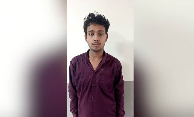 Young man with dark hair and a maroon shirt standing against a plain white background.