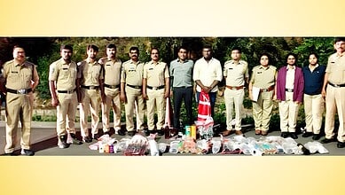 Group of police officers and officials standing outdoors with confiscated items displayed in front.