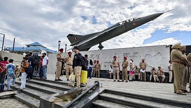 Indian Air Force fighter jet displayed at a public event with police and civilians nearby.