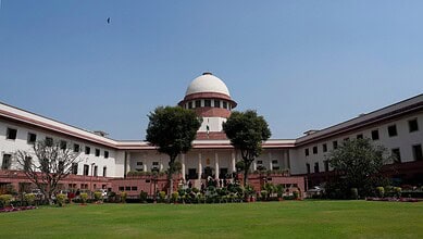 Supreme Court of India building with lush green lawn and trees in front.