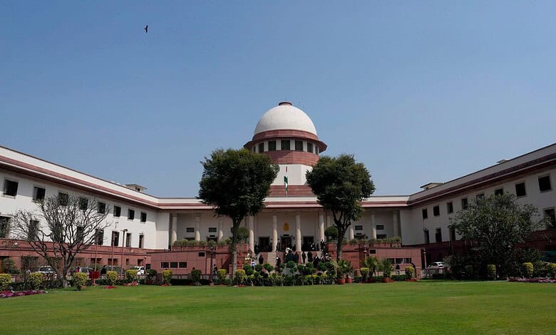 Supreme Court of India building with lush green lawn and trees in front.