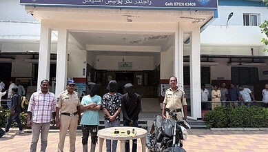 People gathered outside a building in Hyderabad, some in uniform, with a table and motorcycle in front.