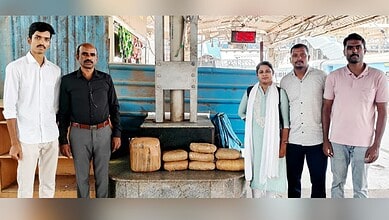 Group of five people standing near a water pump with loaves of bread at a station.