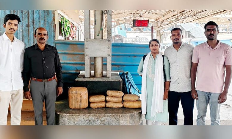 Group of five people standing near a water pump with loaves of bread at a station.