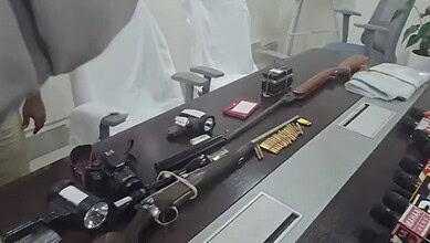 Collection of firearms, ammunition, and related equipment on a conference table.