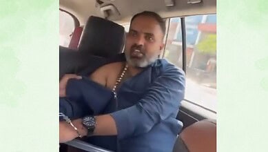 Man with a beard and traditional attire sitting in a vehicle, looking towards the camera.
