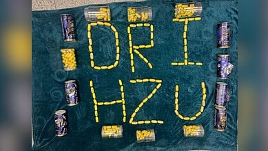 Creative arrangement of yellow and purple cans spelling 'DRI HZU' on a teal surface.
