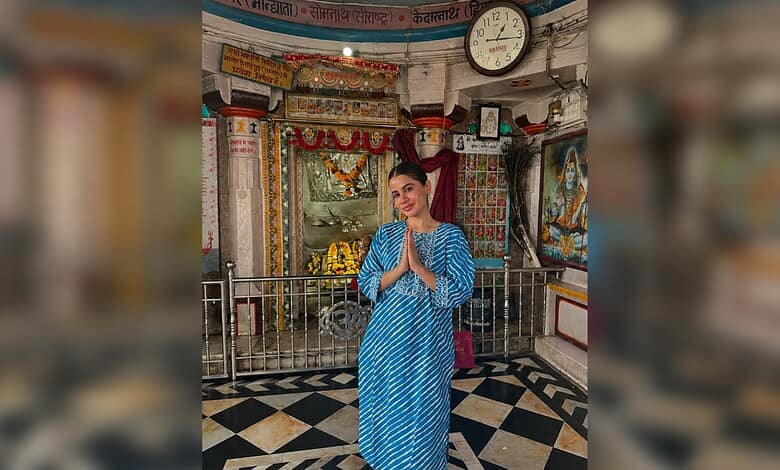 Uorfi Javed in a blue traditional dress praying inside a temple with religious decorations.