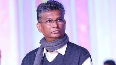Satish Jarkiholi in a formal setting with a grey scarf and glasses.