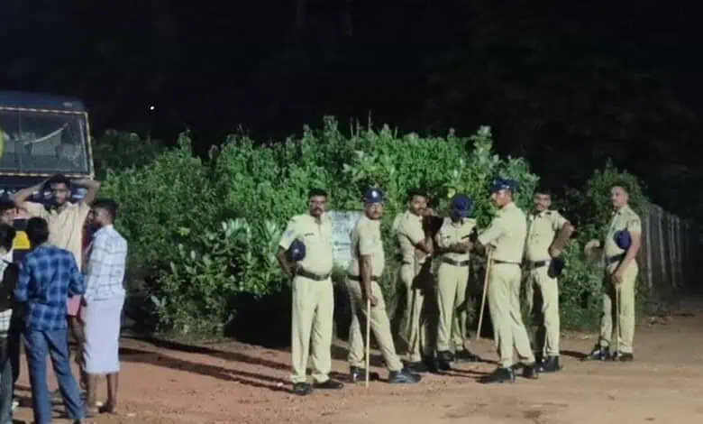 Group of police officers and civilians gathered near bushes during night time.