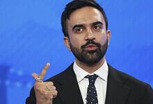 Man in suit gesturing with his index finger against a blue background.