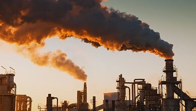 Industrial factory emitting thick black smoke into the sky at sunset.