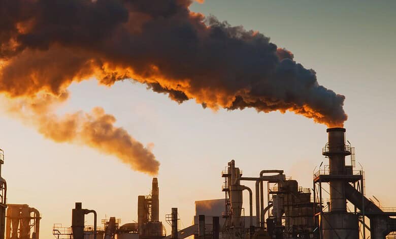 Industrial factory emitting thick black smoke into the sky at sunset.