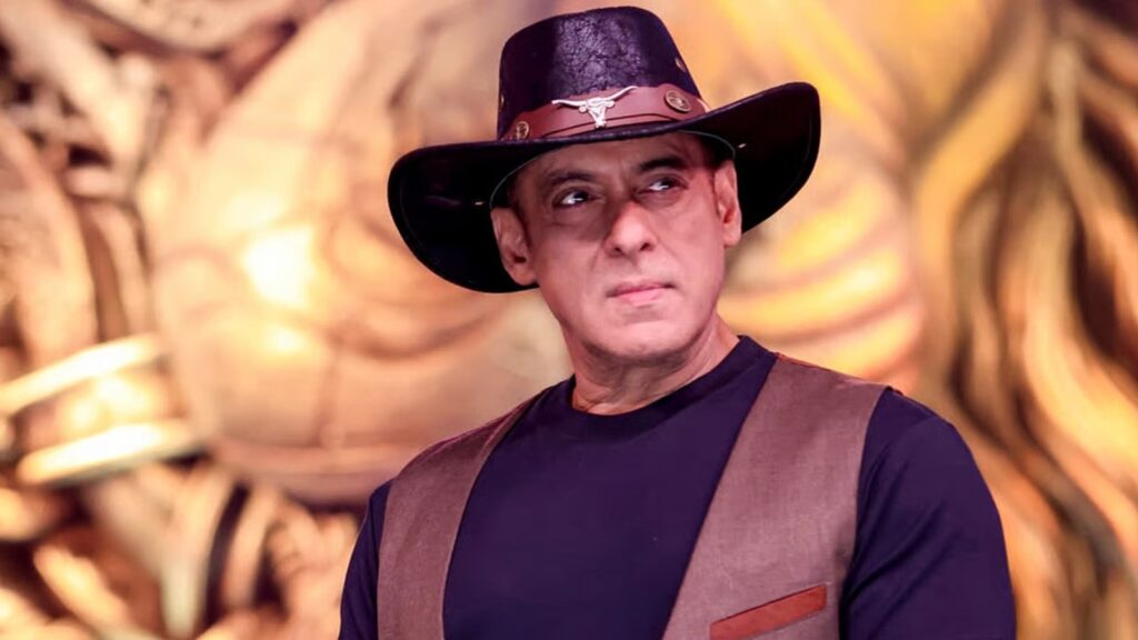 Indian man wearing a black hat with a silver emblem and a brown vest, looking serious.