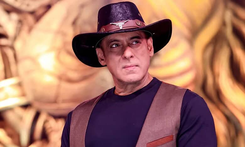 Indian man wearing a black hat with a silver emblem and a brown vest, looking serious.