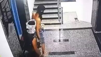 Two men with covered faces entering a building through a glass door.