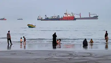 Large oil tanker sailing through the Strait of Hormuz with smaller boats nearby.