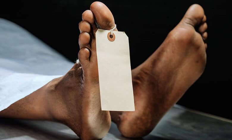 Dead body with a tag attached, lying on a surface in a crime scene or medical setting.