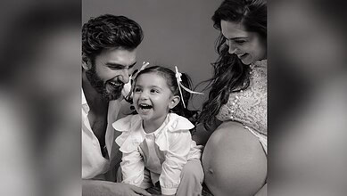 Happy family with a pregnant woman, a man, and a young girl smiling together.