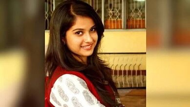 Young woman with long dark hair smiling indoors, wearing a red and white outfit.