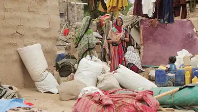 Yemeni refugees in a crowded camp with bags, children, and makeshift shelters.