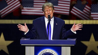 Donald Trump speaking at a rally with American flags in the background.