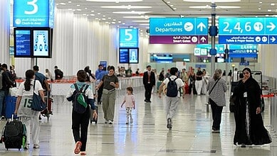 People walking through Dubai Airport terminal with signs for departures and gates.