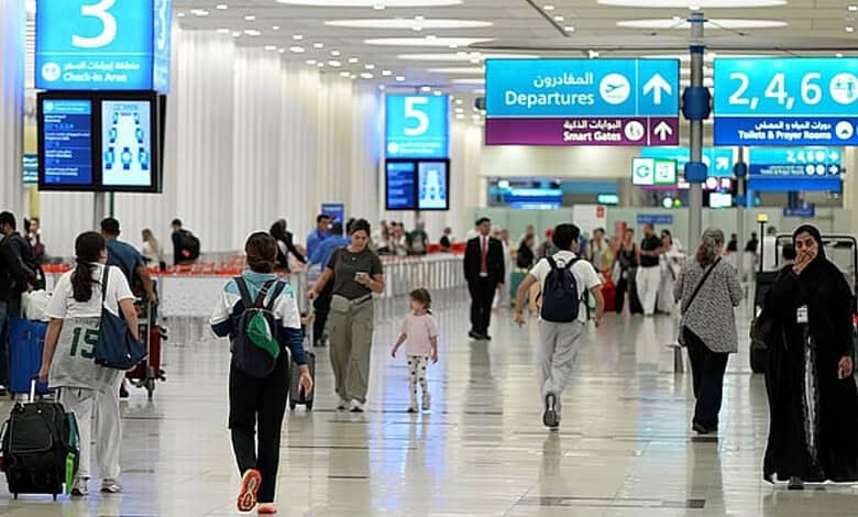 People walking through Dubai Airport terminal with signs for departures and gates.