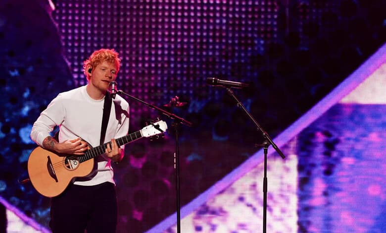 Ed Sheeran playing guitar and singing on stage during a concert.