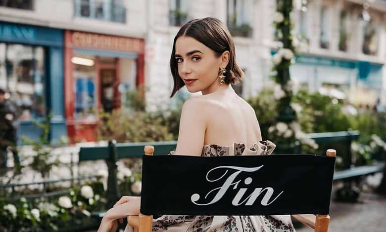Lily Collins with dark hair and elegant makeup, sitting outdoors with a 'Fin' sign.