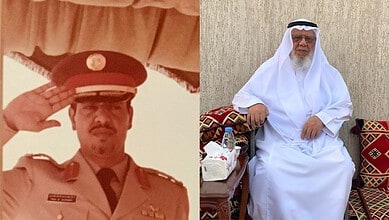 Saudi man in white thobe and head covering sitting on decorated cushions.
