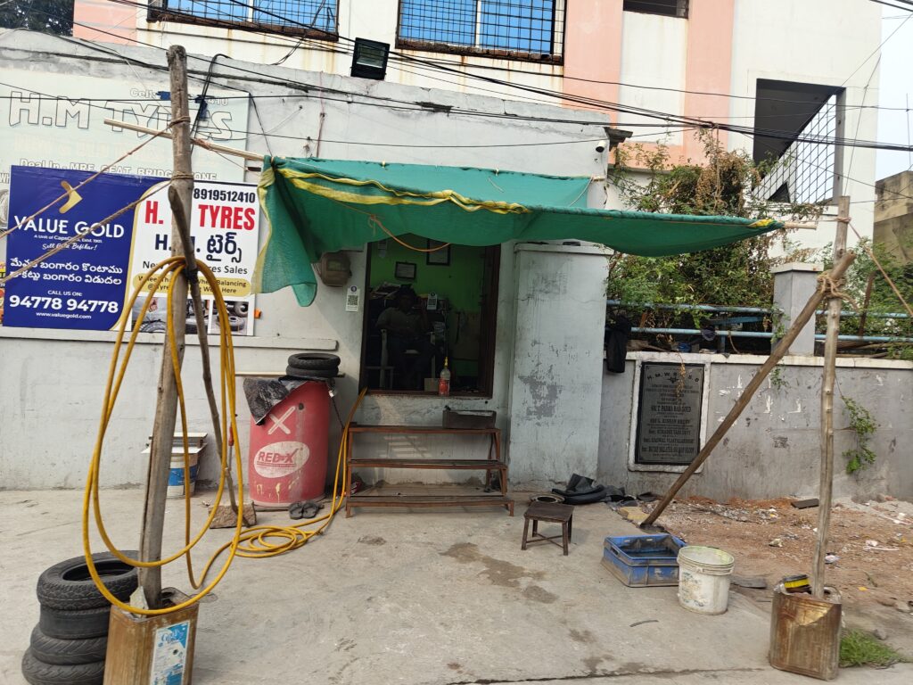 Small roadside shop with green canopy, tyres, and tools in Secunderabad.