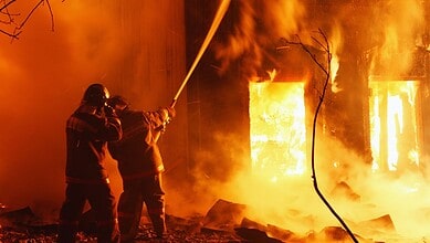 Firefighters combat a large blaze engulfing a building with intense flames and thick smoke.