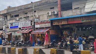 Vendors and shoppers on a busy footpath in the old city with shops and motorcycles.