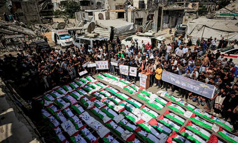 Bodies wrapped in Palestinian flags laid out during a mass funeral in Gaza City’s Al-Zaytoun neighbourhood, surrounded by mourners and war-damaged buildings.